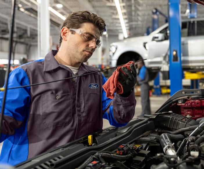 Ford technician checks the engine oil dipstick during an oil change inside a dealership service bay.