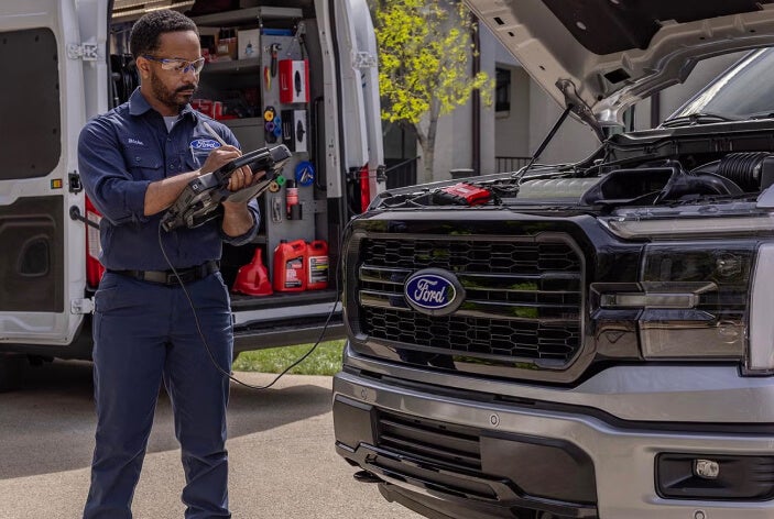 Ford Mobile Service technician performs engine diagnostics on a pickup with the hood open beside a service van.
