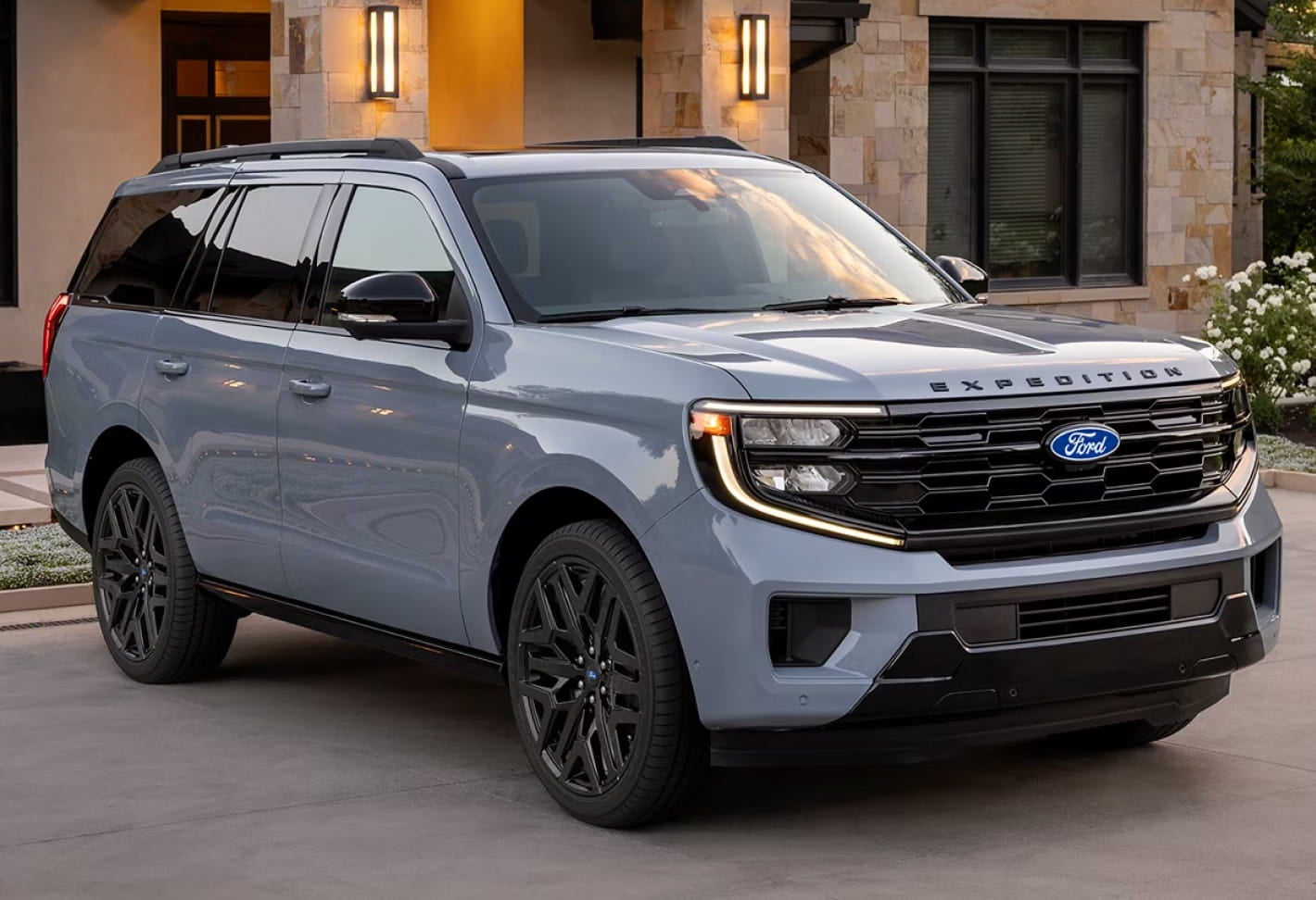 Light blue Ford Expedition SUV parked in the driveway of a modern home with stone exterior walls and landscaped surroundings.