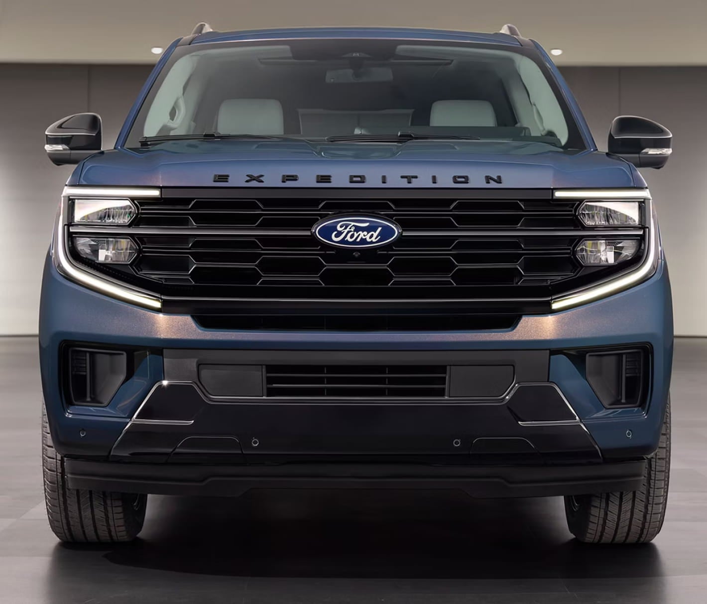Front view of a blue Ford Expedition SUV highlighting the black grille, LED headlights, and bold front-end design in a modern indoor setting.