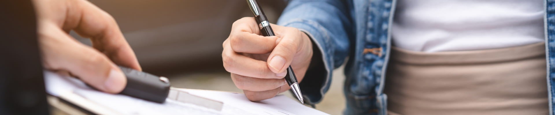 Close-up of a customer signing paperwork while another person holds a car key fob.